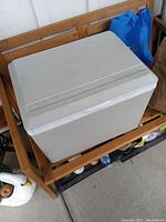 Front and top view of the white portable electric thermoelectric cooler/warmer placed on a wooden bench.