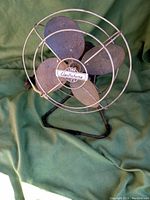 Full view of the 1950s Electrohome Long Life fan showing metal blades, wire cage, and metal stand with erosion and wear.