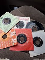 Photo showing six vintage 45 RPM vinyl records, some in paper sleeves with visible labels including Columbia and RCA Victor.