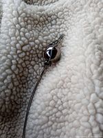 Close-up of the polished round silver harmony ball pendant that jingles when shaken, attached to a thin snake chain with a decorative clasp.