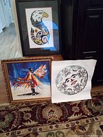 Framed Ron LaRochelle eagle print, original unsigned dancer painting, and framed Burton Amos moon print on ornate carpet.