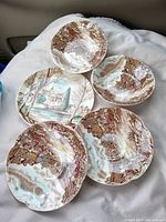 Photo showing six small ceramic dishes decorated with Dream Town and Old English countryside village scenes in earthy colors, arranged on a white cloth.