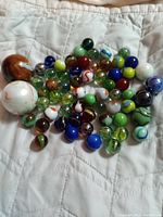Photo showing an assortment of various sized marbles with many colors and swirl designs laid out on a light-colored quilted fabric.