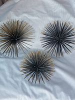 Three metal atomic burst decor pieces shown from the front on white fabric background.