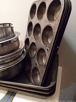 Stack of black metal baking pans including cupcake tins and lasagne pans.