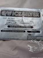 Front side of Qwicksilver cleaning plate package with logo and description stating it is a self-acting electrolytic cleaning plate for silver, silver plate, copper, bronze, gold, jewelry, stainless steel, and brass.