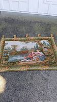 Full view of vintage French tapestry laid flat outdoors, showing the entire scenic and ornate border design.