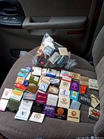 Photo of approximately 40 matchbooks arranged on a car seat, featuring various vintage designs from hotels, casinos, restaurants, and local businesses primarily in Hawaiian, Las Vegas, and B.C. locations.