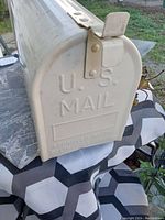 Photo of the mailbox showing embossed 'U.S. MAIL' text and partial flag at the side.