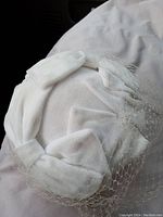 Close-up of the top and side of the white velvet hat showing decorative bows and veil netting.