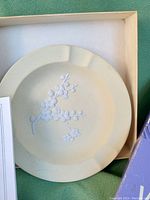 Close-up of the primrose yellow Jasperware dish showing the white Prunus blossom relief on the inside center with a slightly matte finish.