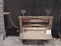 Front view of the antique clothes wringer showing wooden rollers, metal frame, hand crank with wooden grip, and adjustment screws on top.