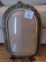 Full view of the antique picture frame showing the arched top, floral carved design, and convex glass surface.