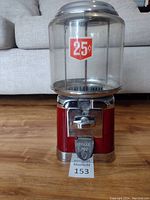 Front view of the red base candy dispenser with chrome details and clear plastic globe showing "25¢" sticker. Visible quarter coin inside mechanism.