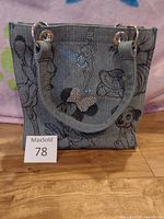 Front view of blue denim-style purse with Disney characters Minnie Mouse, Tinkerbell, and a Dalmatian dog printed and embroidered on the exterior.