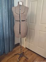 Full view of antique dress maker mannequin, mounted on metal stand, fabric covered with front opening adjustable sections.