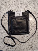 Front view of black Fossil leather purse with zippered front pocket and long strap