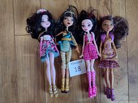 Full view of all four Monster High dolls lying on wood floor showing outfits and size.