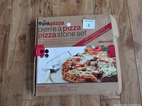 Closed box with packaging showing the ThinkKitchen pizza stone set label and a picture of a pizza on the stone.