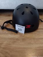 Black skateboard or bike helmet shown from side view on wooden floor with MaxSold tag 59