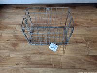 Top angle view of metal folding milk crate on wooden floor, showing wire grid construction and open folding panels.