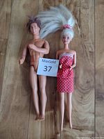 Front view of Barbie and Ken dolls standing on wooden floor, showing body and outfits