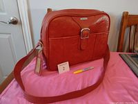 Photo showing front and side view of the vintage Samsonite carry on bag placed on a pink cloth, highlighting the buckle front pocket and luggage tag.