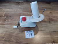 White plastic manual wool winder placed on wooden surface with visible crank handle, clamp for table attachment, and a red tension knob.