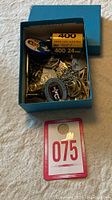 Box of assorted jewelry, pins, keychains and a film roll container shown in a blue box.