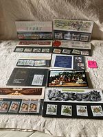 Top down image of 9 diverse United Kingdom mint stamps presentation packs laid out on fabric, showing themes like sport, Victorian Britain, medieval life, and historical events. Most appear sealed.