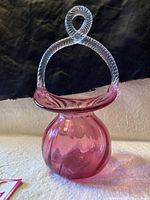 Side view of cranberry glass basket vase showing twisted clear glass handle and rounded cranberry glass body.
