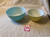 Two Pyrex mixing bowls side by side on a beige fabric surface. Yellow smaller bowl and turquoise larger bowl visible.