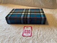 Closed blue tartan plaid shortbread tin displayed on fabric surface with auction lot number card