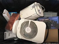 Photo shows two white fans, white round fan and rectangular fan, plus a set of LED rock lights in box and various electronic accessories.