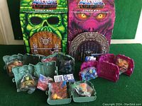 Photo showing two large colorful cardboard cutouts with distinct Enternia themes and six green cases displayed in front containing mini figures sealed in plastic bags.