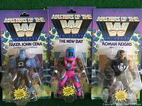 Front view of three Masters of the Universe figures in packaging: Faker John Cena, The New Day, and Roman Reigns.