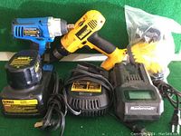 DeWalt cordless drill with battery attached, two DeWalt chargers, one Mastercraft charger, and bag of accessories arranged on green surface.