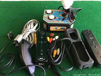 Photo showing Ms. Pac-Man arcade style plug-in video game console beside Nintendo Wii controllers and cables on green surface.