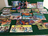 Full view of vintage Masters of the Universe card backs, mini comics, character standees, and two action figures placed on green cloth.