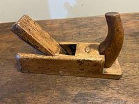 Side view of antique wooden smoothing plane showing wooden handle and blade angle.