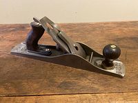 Side angle of the entire Stanley Bailey No.5 jack plane showing the metal body with rosewood front knob and wood rear handle, placed on a wooden surface.