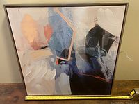 Front view of abstract canvas painting with blue, peach, cream, black colors and geometric brush strokes.