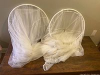 Two IKEA bed canopy rings draped with white sheer netting fabric resting on a wooden table.