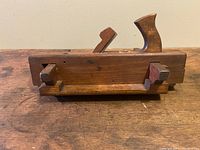 Side view of the antique wooden plow molding plane, showing the full length of the tool with wooden handles and blade positioned underneath.