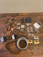 Full lot overview showing assorted metal hinges, screws in container, a white metal handle, and various metal brackets and plates on wooden background.