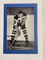 Front side of vintage black and white photo showing Bobby Bauer in hockey uniform number 8, lithographed or signed on the lower right area, mounted on blue cardstock.
