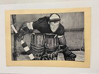 Front side of black and white photo showing Norman E. Smith in full goalie gear posing in front of a hockey net, featuring printed signature.