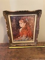 Frontal view of the framed oil painting showing the young girl with long red hair and lace dress seated, framed in an ornate carved wooden frame with chipping.