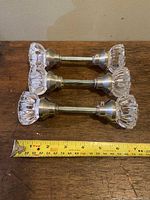 Three vintage glass handled door knobs arranged flat on a wooden surface with a measuring tape showing just under 6 inches in length for scale.