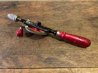 Side angle view of the vintage Hoppe egg beater hand drill showing the handle, crank, and chuck against a wooden surface.